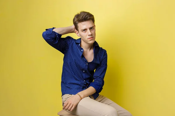 Jonge man in een blauw shirt, die hand op achterkant van het hoofd, iets vergeten of gevoel van verdriet, zittend over gele muur van streek — Stockfoto