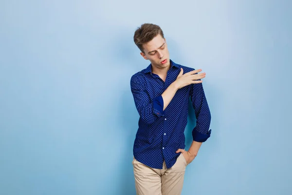 ブルーの壁に立っている間彼の肩からほこりを振る青いシャツを着ているハンサムな若い男の肖像 — ストック写真