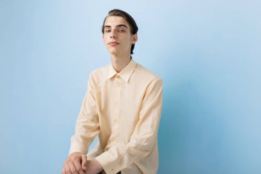 Mavi duvarın üzerinden poz sarı gömlek giymiş mavi gözlü yakışıklı genç ince esmer çocuk