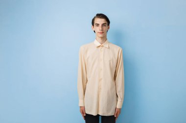 Mavi duvarın üzerinden poz sarı gömlek giymiş mavi gözlü yakışıklı genç ince esmer çocuk