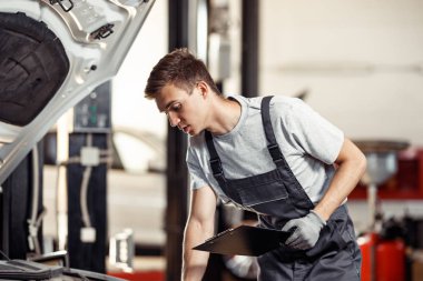 Genç bir automechanic bir araba servisinde çalışmalarının sonuçları kontrol ediyor