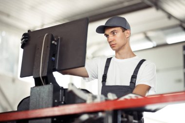 Mavi gözlü genç bir mekanik bir araba bir bilgisayar kullanarak bir araba servisinde kontrol ediyor