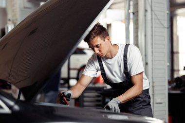 Bir genç ve uyumlu mekanik bir araba servisi, işini yapıyor: onun çalışma sonuçlarını denetleme