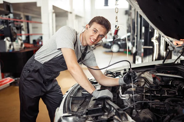Ein gut aussehender Mechaniker lächelt bei der Überprüfung eines Motors — Stockfoto