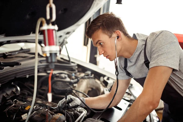 Ein junger gelernter Mechaniker sucht Käfer bei einem Autoservice — Stockfoto
