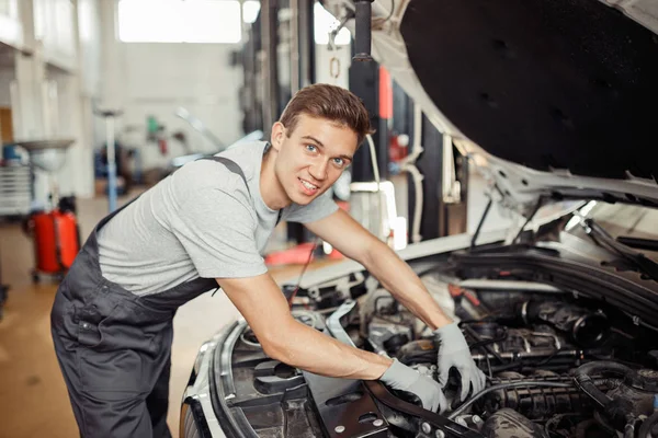 Ein junger gutaussehender Mann überprüft den Motor eines Autos bei einem Autoservice — Stockfoto