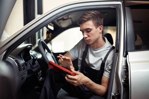 Verificar um carro no autoservice: um jovem mecânico está à procura de bugs — Fotografia de Stock