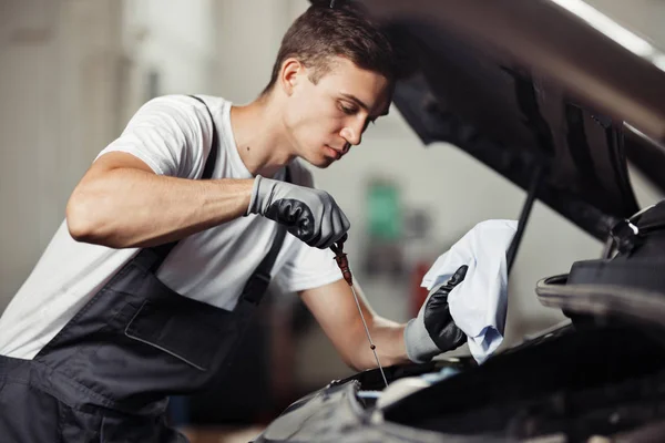Un mecánico joven y atractivo está comprobando el nivel de aceite de un motor de coche — Foto de Stock