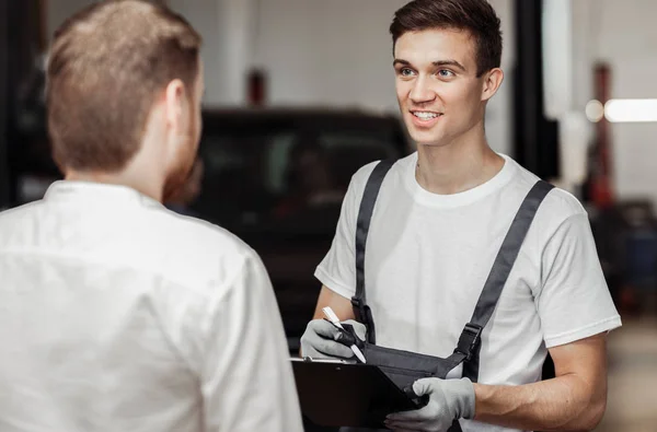 Un mécanicien automobile sourit à son client et l'invite à regarder sa voiture — Photo