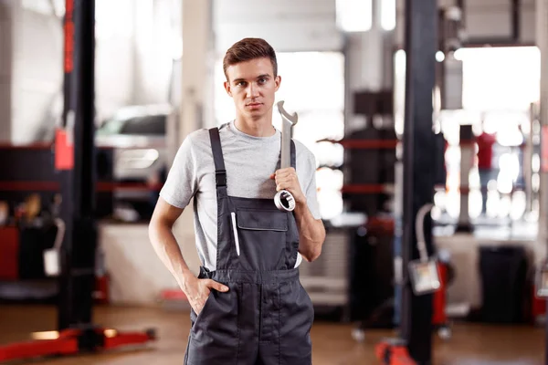Yakışıklı bir automechanic elinde bir anahtar ile bir araba onarım servisinde duruyor — Stok fotoğraf