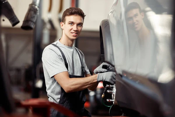 A smiling car mechanic is fixing a lifted car