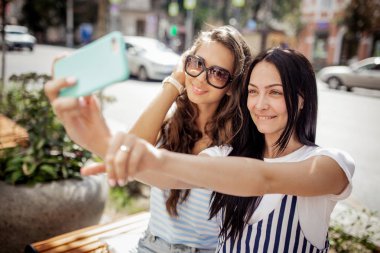 İki çok ince kız rahat stil içinde giyinmiş, uzun siyah saçlı tezgah oturup bir selfie,