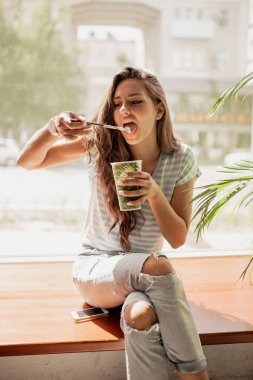 Çok ince bir genç kız gündelik kıyafeti, pencere ve içecekler kahve rahat bir kafede oturup giymiş uzun saçlı.