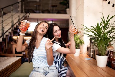 Oldukça genç kızlar, gündelik kıyafeti giymiş gülümseyen iki yan yana oturup rahat bir kafede kameraya bakmak.