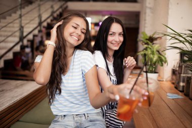 Oldukça genç kızlar, gündelik kıyafeti giymiş gülümseyen iki yan yana oturup rahat bir kafede kameraya bakmak.