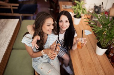 Koyu saçlı, gündelik kıyafeti giymiş iki güzel genç gülümseyen kız birbirlerine sıcak bir kahve dükkanında sarılmak.