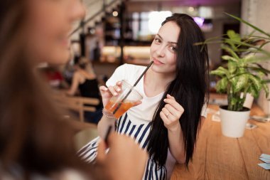 İki güzel genç gülümseyen kız siyah saçlı, gündelik kıyafeti giymiş ve karşılıklı stand rahat bir kafede sohbet.