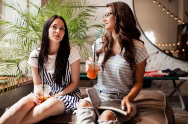 Uzun siyah saçlı, iki genç güzel kız Casual elbiseler giymiş yan yana oturmak ve modern bir kafede kahve içmek. .