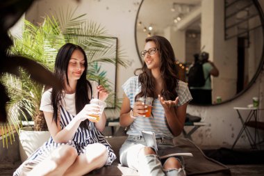 Uzun siyah saçlı, iki genç güzel kız Casual elbiseler giymiş yan yana oturmak ve modern bir kafede kahve içmek.