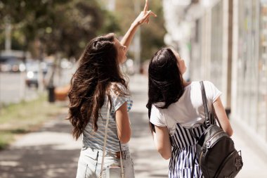 Uzun siyah saçlı iki dostu sevimli kız gündelik kıyafeti giymiş sokakta yürürken ve el ele.