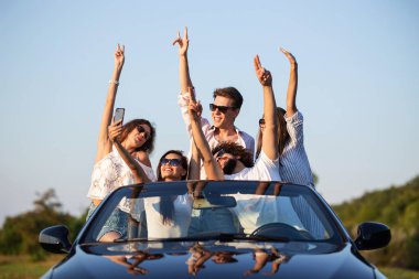 Şanslı genç kızlar ve erkekler için güneş gözlüğü siyah Cabriolet ellerini tutarak ve selfie güneşli bir günde yapma yolu üzerinde oturan.