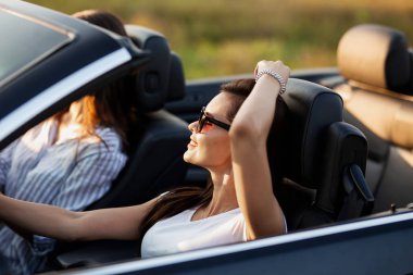 Muhteşem genç esmer genç kadın bir cabriolet oturan ve gülümseyen güneşli bir günde beyaz tişört giymiş güneş gözlüğü.