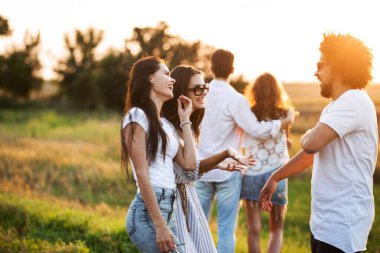 İki genç kadın kıvırcık olan genç adam açık sohbet. Arka planda bir genç bir kız kucaklar..