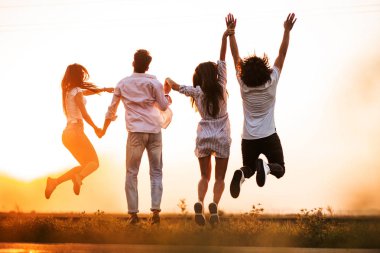 İki genç çocuklar ve iki kız onların elini tutarak ve bir yaz gününde alanında atlama. Arkadan görünüm.