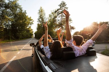 Şirket bir cabriolet yolda sürme ve sıcak güneşli bir günde ellerini dayanabiliyor gençlerin. Arkadan görünüm.