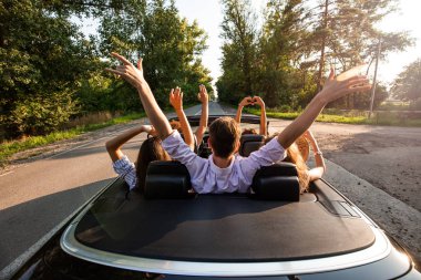  bir cabriolet yolda sürme ve sıcak güneşli bir günde ellerini dayanabiliyor gençlerin irkette. Arkadan görünüm.
