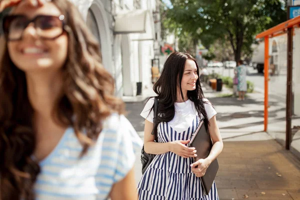 Duas lindas garotas com cabelos longos e escuros, vestindo roupas casuais, caminham pela rua em um dia ensolarado , — Fotografia de Stock