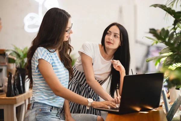 To søte, slanke jenter med langt, mørkt hår, med uformell stil, sitter ved bordet og ser på hverandre i en koselig kaffebar . – stockfoto