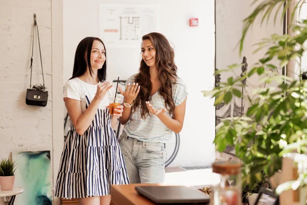 Δύο νέοι χαμογελώντας λεπτές κορίτσια με μακριά σκούρα μαλλιά συνομιλούν μεταξύ τους σε ένα άνετο κατάστημα καφέ. — Φωτογραφία Αρχείου