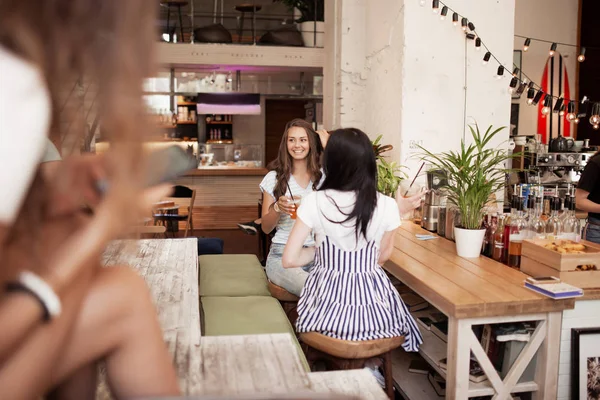 Due ragazze carine e magre dai capelli scuri, che indossano uno stile casual, si siedono di fronte all'altro e chiacchierano in un'accogliente caffetteria . — Foto Stock