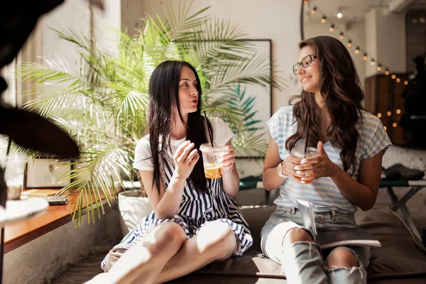 两个长着黑发的年轻美女, 穿着休闲的衣服, 坐在旁边, 在一家现代化的咖啡店里喝咖啡. — 图库照片