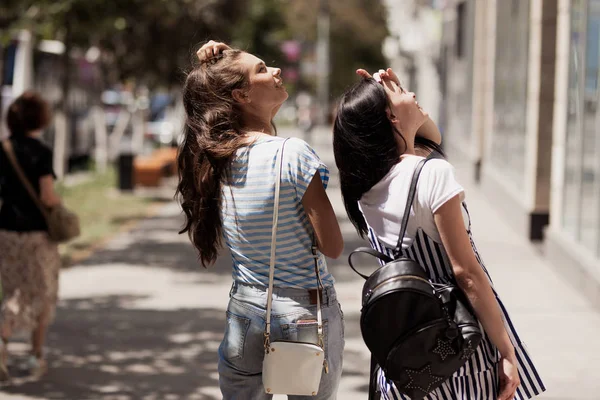 Twee jonge leuke slanke meisjes met lang haar, lopen in de straat op een zonnige dag. — Stockfoto