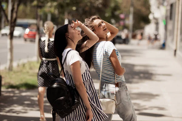 Twee jonge leuke slanke meisjes met lang haar, lopen in de straat op een zonnige dag. — Stockfoto