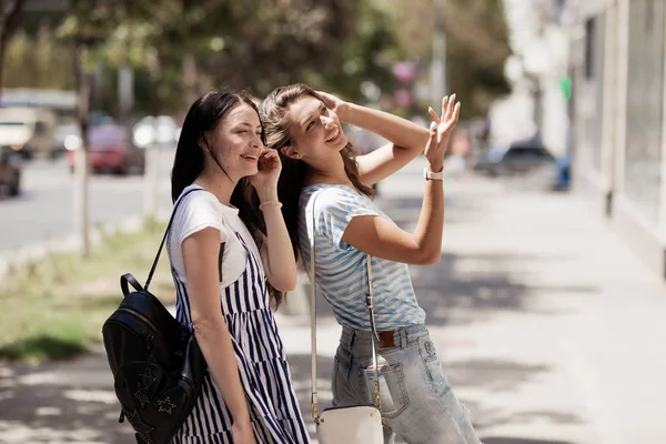 Deux jeunes filles minces et mignonnes aux cheveux longs, marchent dans la rue par une journée ensoleillée . — Photo