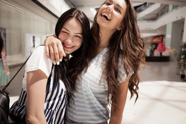 Två unga ganska mörkhårig flickor, bär casual outfit, krama varandra i en lobby. — Stockfoto