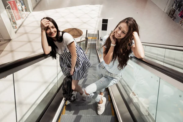 Twee jonge vrij slanke meisjes, het dragen van casual stijl, staan naast elkaar op de roltrap. — Stockfoto