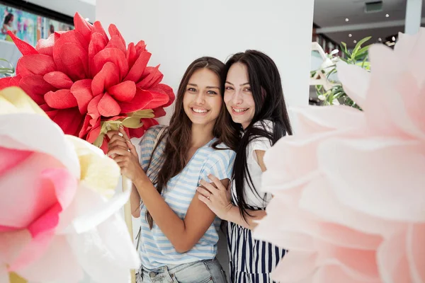 Zwei jugendlich lächelnde schlanke Mädchen in lässigem Outfit stehen nebeneinander in der Lobby eines modernen Einkaufszentrums, — Stockfoto