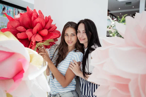 Zwei jugendlich lächelnde schlanke Mädchen in lässigem Outfit stehen nebeneinander in der Lobby eines modernen Einkaufszentrums, — Stockfoto