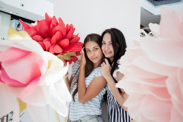 Twee jeugdige slanke meisjes, gekleed in een casual outfit, glimlachend staan naast elkaar in een hal van een modern winkelcentrum, — Stockfoto