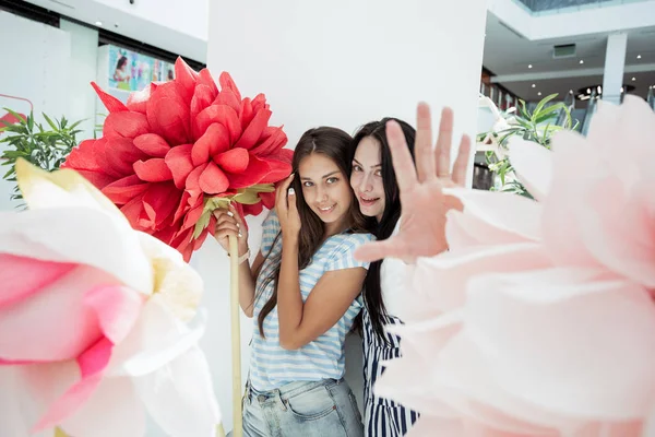 Zwei jugendlich lächelnde schlanke Mädchen in lässigem Outfit stehen nebeneinander in der Lobby eines modernen Einkaufszentrums, — Stockfoto