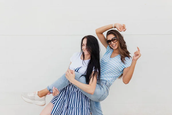 Dos jóvenes y delgadas damas de cabello oscuro, vestidas con ropa casual, se paran una al lado de la otra y posan en la calle. . — Foto de Stock