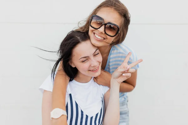 Två ungdomliga mörkhåriga tjejer, bär casual outfit, härlig kram varandra och tittar på kameran. — Stockfoto