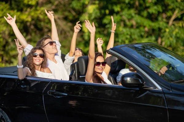 Caras bonitos em roupas brancas e óculos de sol estão sentados em um cabriolet preto e segurando as mãos para cima em um dia ensolarado . — Fotografia de Stock