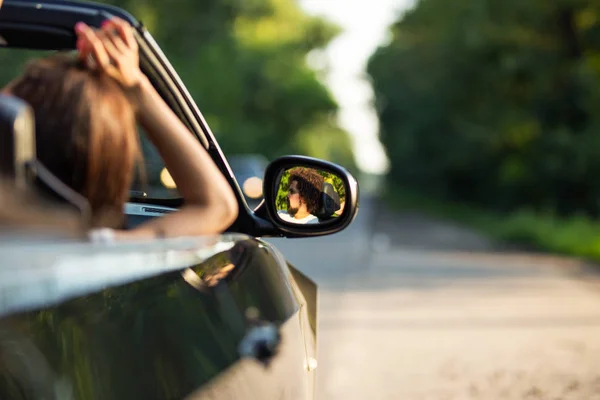 Cabriolet noir sur la route par une journée ensoleillée. Dans le miroir latéral est le reflet du jeune homme brun avec la barbe . — Photo