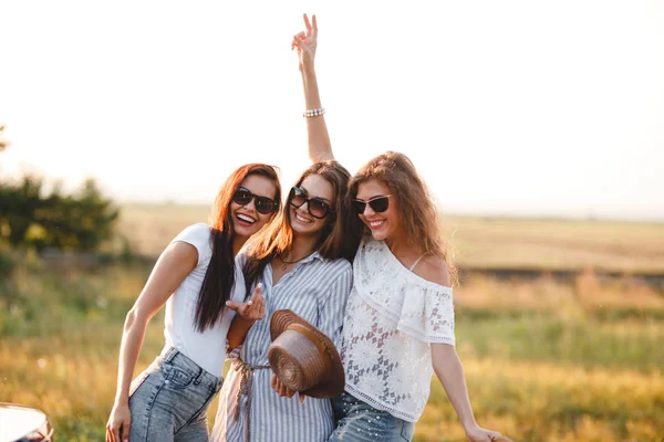 Tre bellissime giovani donne in occhiali da sole in piedi nel campo e sorridente in una giornata di sole . — Foto Stock