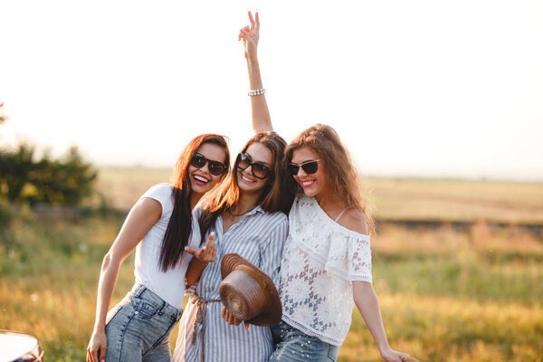 Three gorgeous young women in sunglasses stand in the field and smiling on a sunny day.